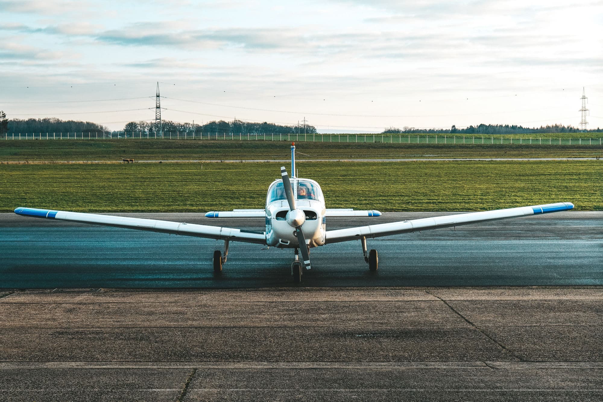 Avioneta blanca y azul vista de frente en la pista de un aeródromo, con campo verde al fondo.